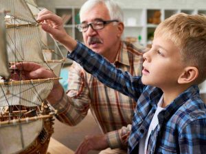 A boy and a elderly man building a sail boat model