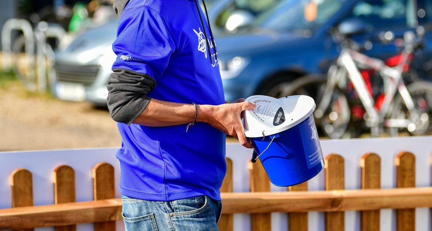Man in blue t-shirt and hat holding donation bucket