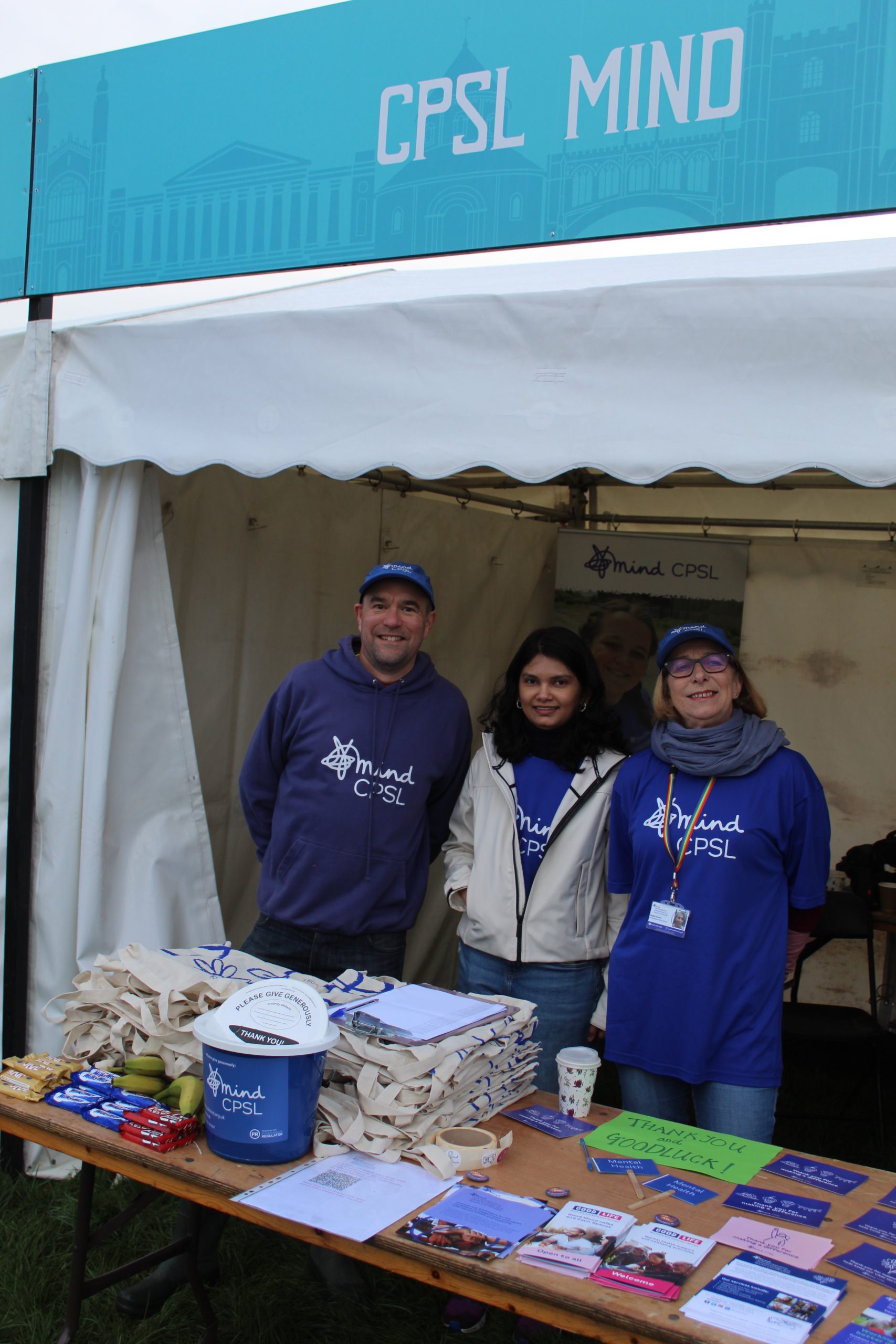 Three staff members of CPSL Mind wearing CPSL Mind t-shirts and standing behind a stall