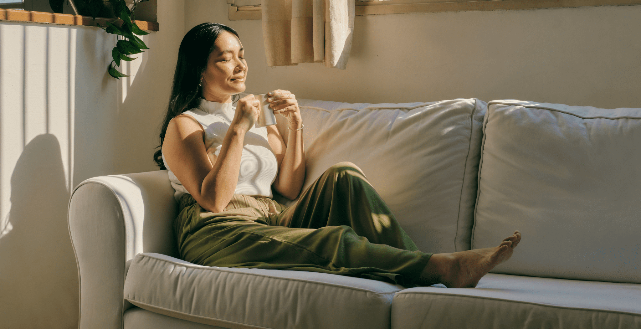 A woman sitting on the couch and drinking a hot beverage - to avoid feeling stressed